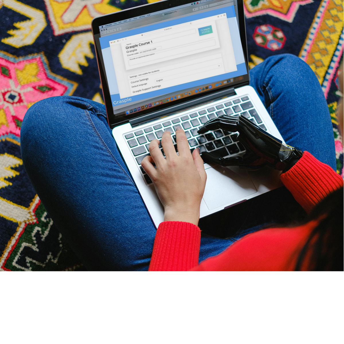 A person is sitting on a colourful carpet. They have a prosthetic right hand and they are navigating the Grasple tool on their laptop with their keyboard.